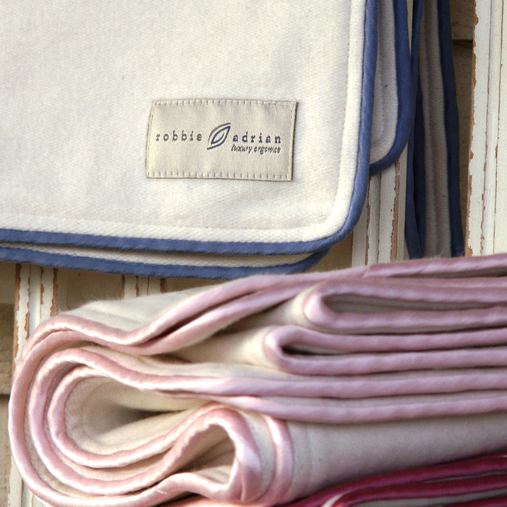 Organic cotton fleece baby blankets with silk piping, label detail and folded stack